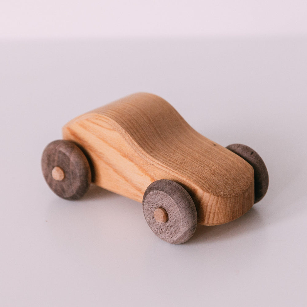 A small wooden toy car with a light colored body and dark wooden wheels.