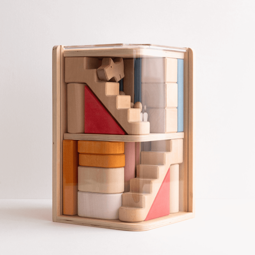 A wooden block set arranged to show a multi-floor structure with various shapes such as stairs and arches, and a small figurine of a family and a dog in a play setting.