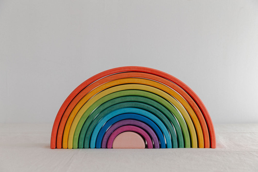 A colorful wooden rainbow stacker toy with multiple arches in various sizes arranged in a spiral pattern on a white background.