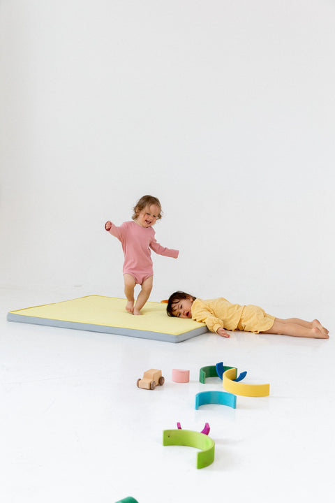 one kid is jumping barefoot while another is bending over the mat