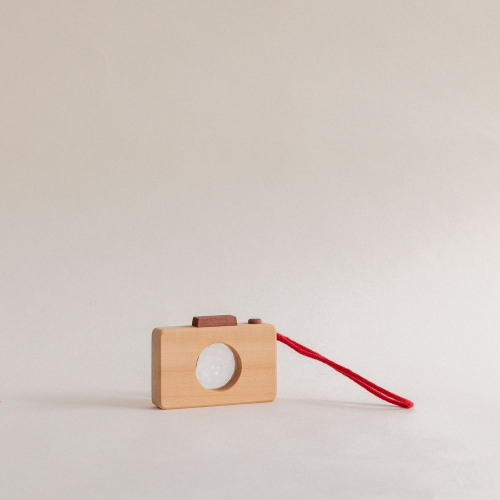 Kaleidoscope camera with a kaleidoscope lens, featuring a solid wood construction and a red strap on a light background.