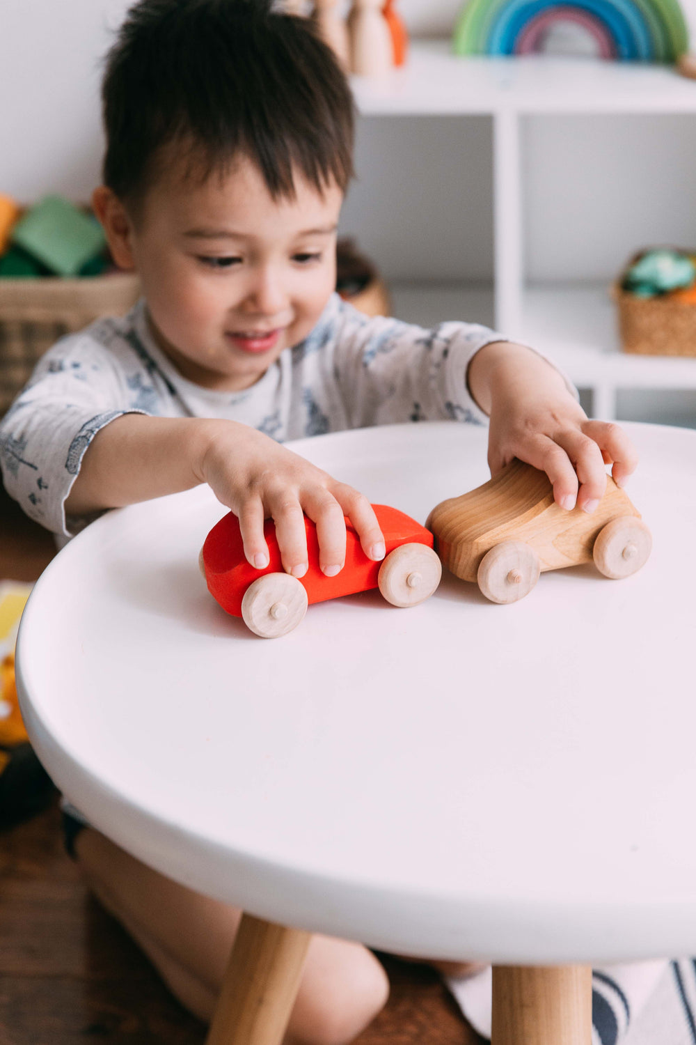 A boy plays two wooden cars on the white coffee table