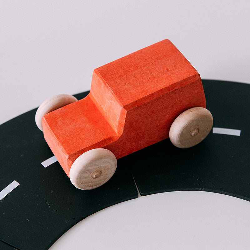 A small red wooden toy jeep with a beige finish and dark gray wheels, displayed on the toy road