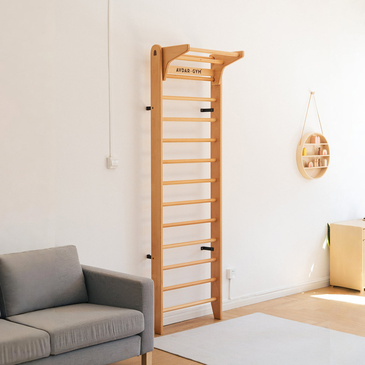 A wooden wall bar set with multiple rungs, mounted on a white wall, with a gray sofa to the left in a home environment.