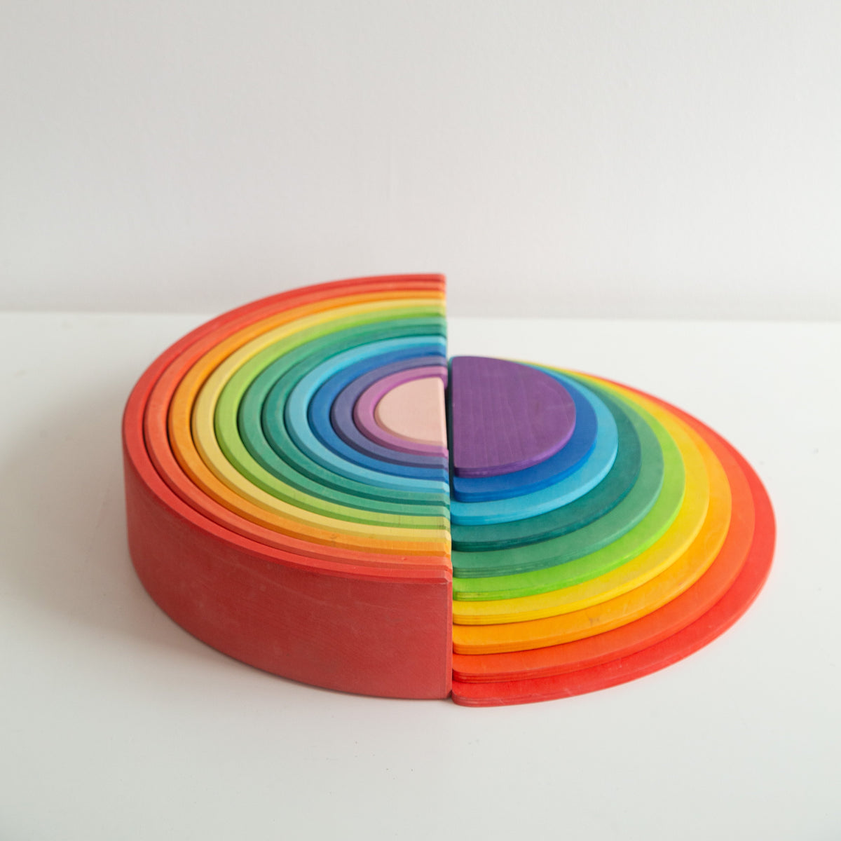 A colorful wooden rainbow stacker toy with multiple arches in various sizes arranged in a spiral pattern on a white background.