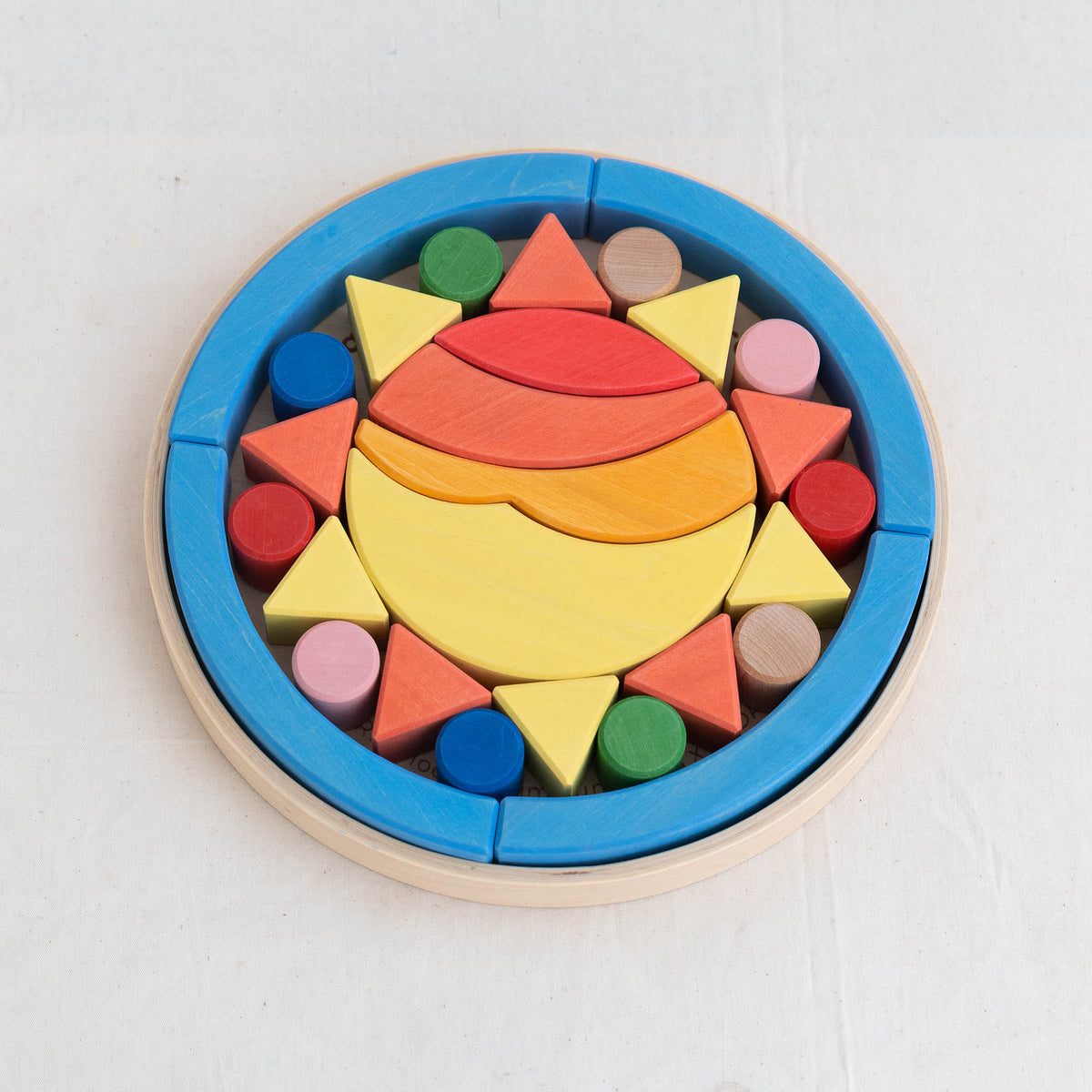 A colorful wooden puzzle block toy with geometric shapes in shades of blue, red, yellow, and green, neatly arranged in a circular pattern with a blue outer rim.