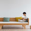 A child leaning on a beige Hug Hug Bed 90x200 , surrounded by pillows of different colors.
