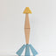 Wooden toy figure with a yellow head, brown torso, and blue legs on a light gray background