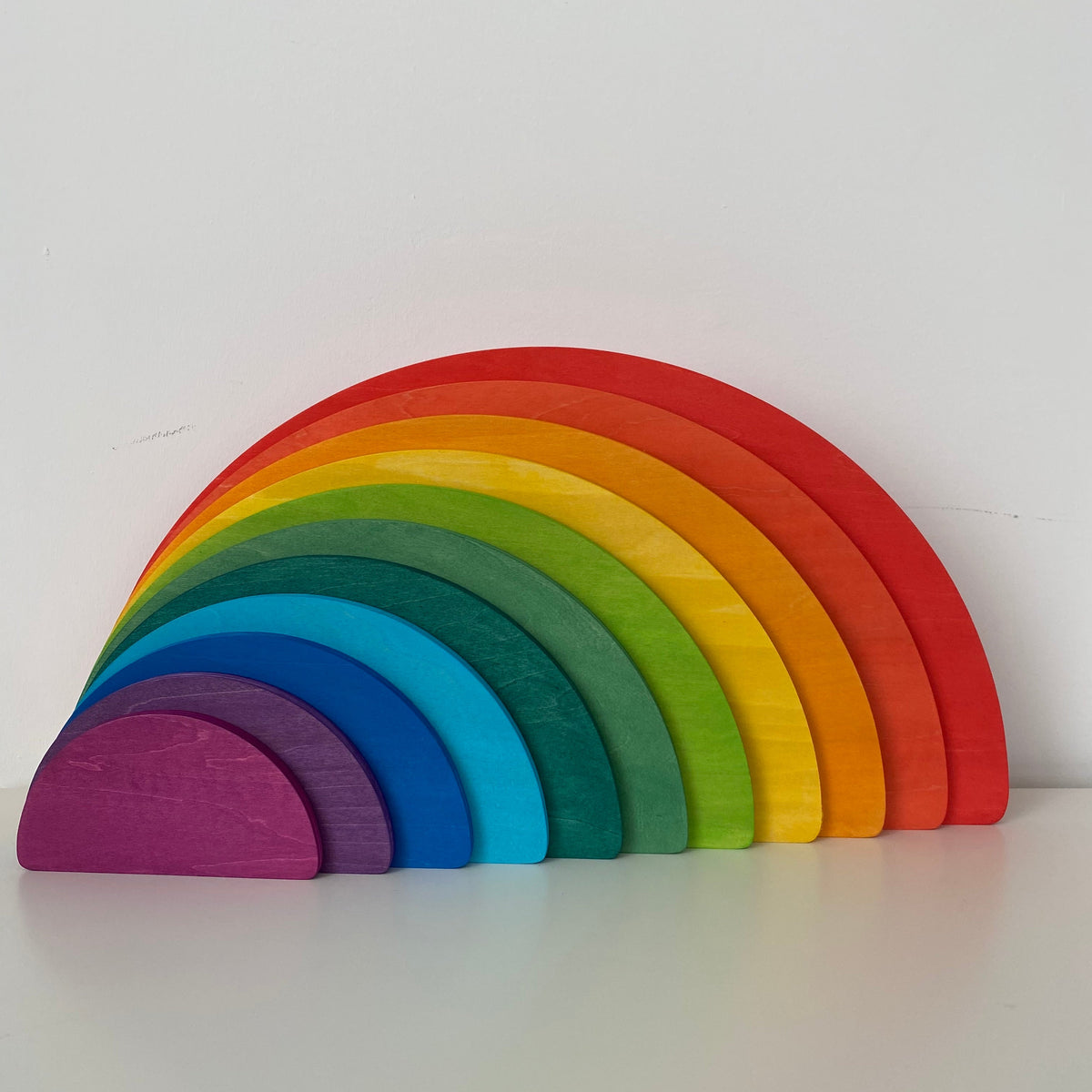 A wooden semicircle stacker toy with rainbow colors displayed on a white background.